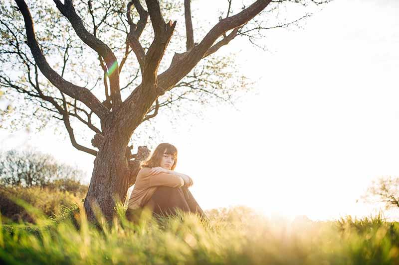 Woman sitting in front of a tree in a field